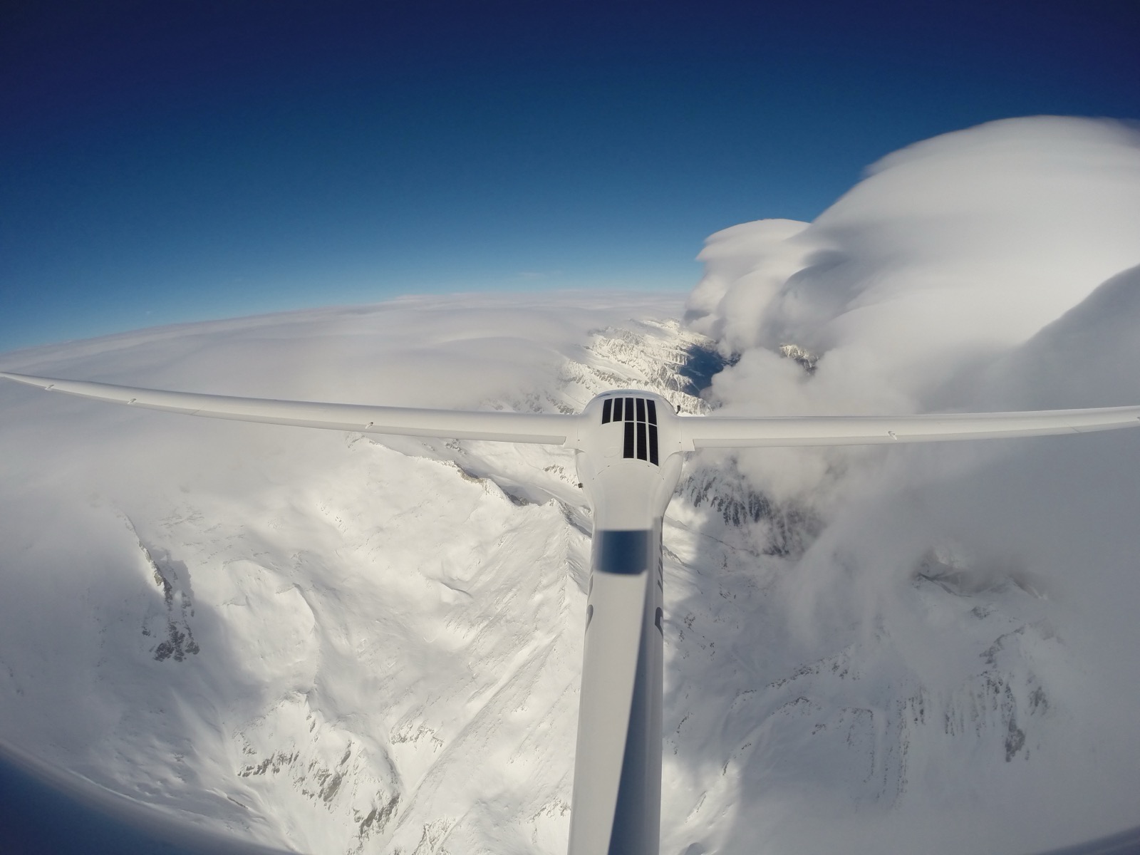 Lenticular clouds towering above a snow-covered ridge, seen from a sailplane.